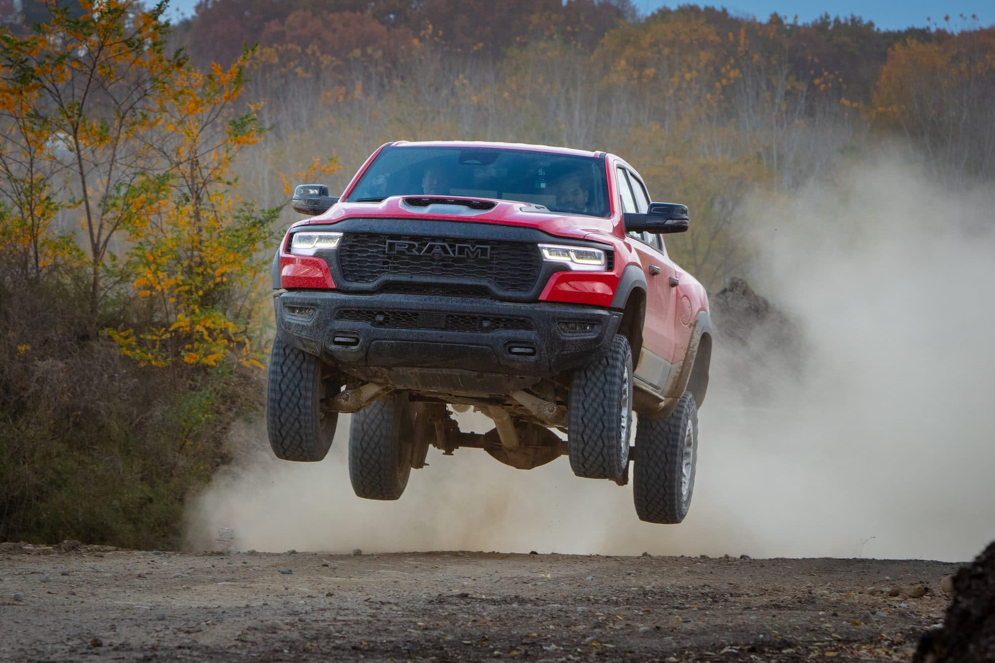 A red 2025 Ram 1500 RHO airborne over a dirt jump, front wheels lifted, dust cloud behind it.
