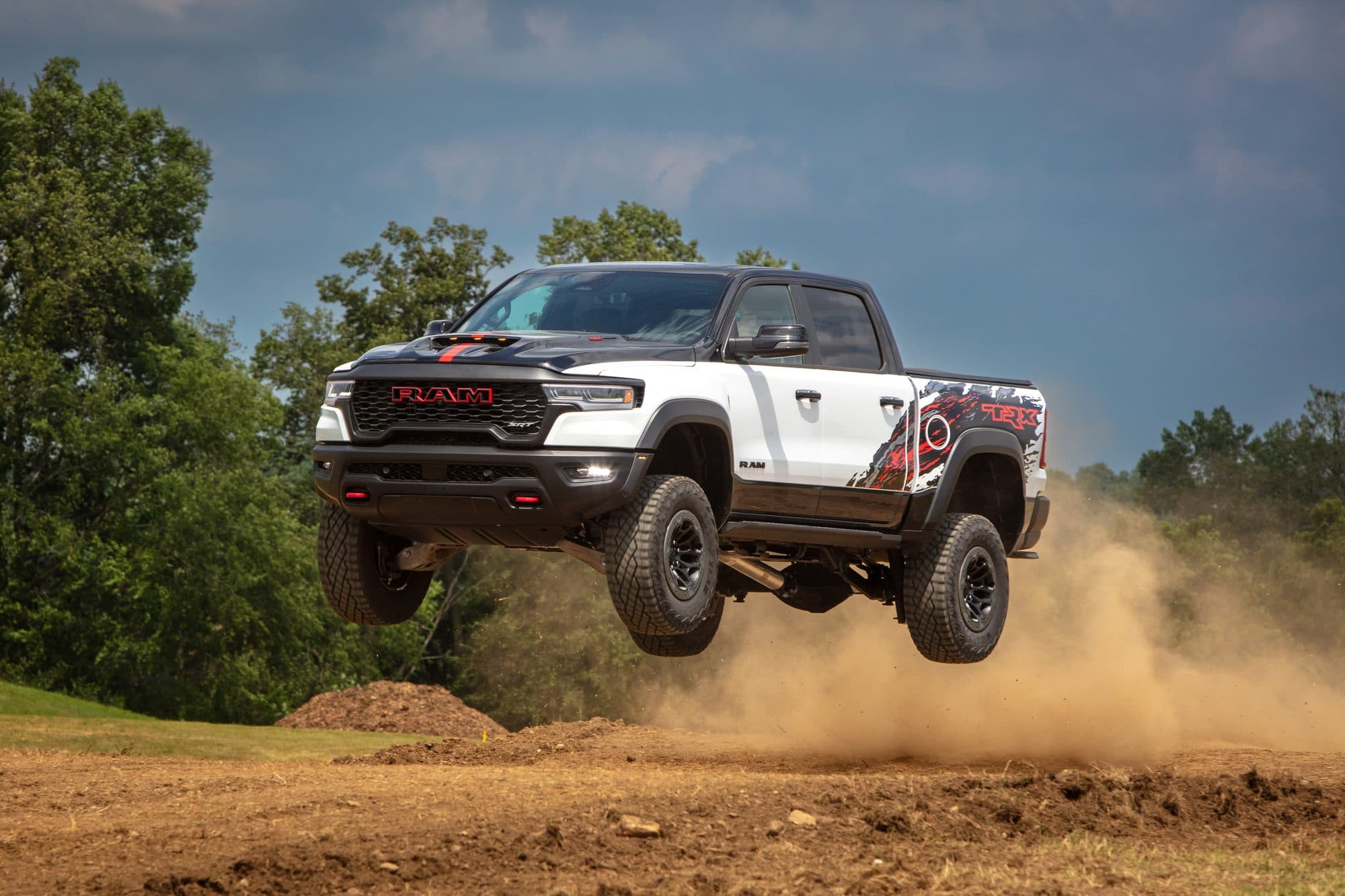 A 2027 Ram 1500 SRT TRX Bloodshot Night edition in Bright White, all four wheels off the ground over a dirt crest with dust trailing behind it.