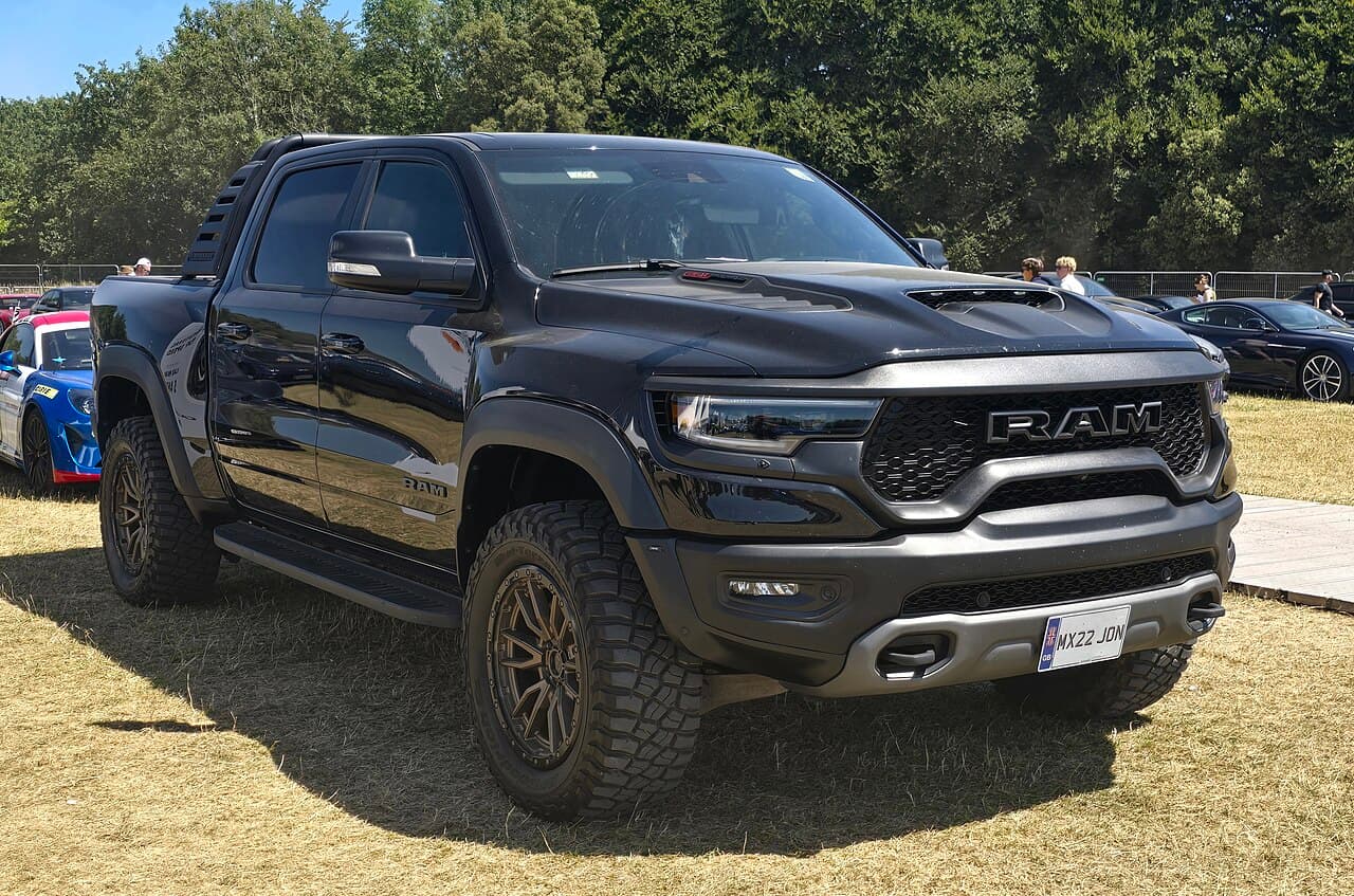 Front three-quarter view of a black Ram 1500 TRX parked under an outdoor show tent next to another dark Ram truck.