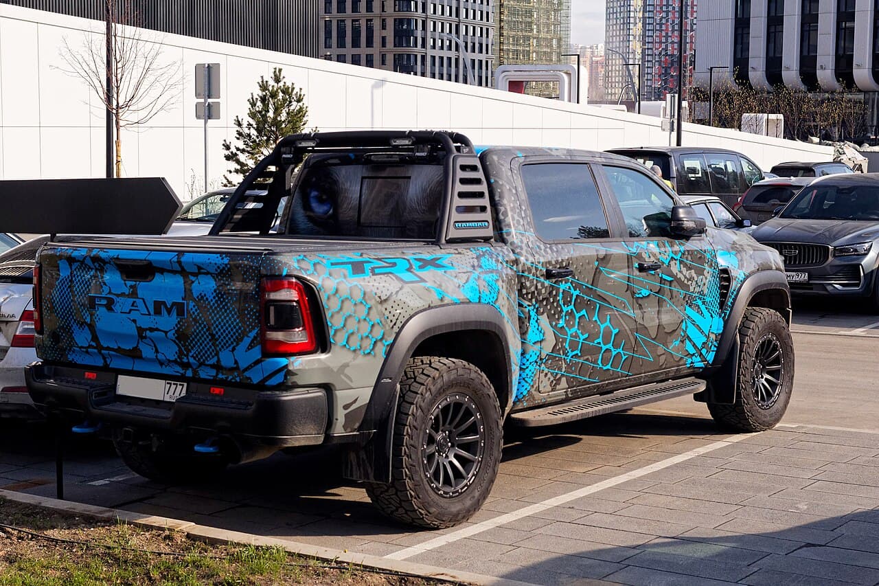 Rear three-quarter view (alternate angle) of the same gray/blue-wrapped Ram 1500 TRX with roll cage and light bar, parked on a Moscow street.