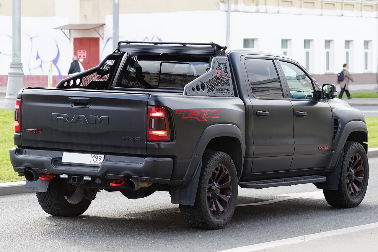 Rear three-quarter view of a matte black Ram 1500 TRX with a large red 'TRX' tailgate decal and an aftermarket bed rack, parked on a Moscow street.
