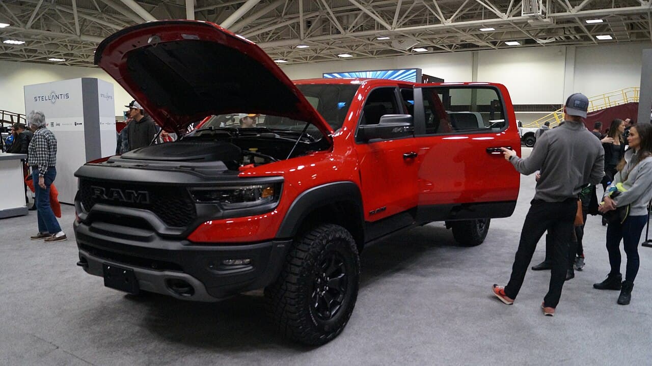 Front three-quarter view of a red Ram 1500 TRX with its hood open at the Twin Cities Auto Show, Minneapolis, next to a Stellantis display.