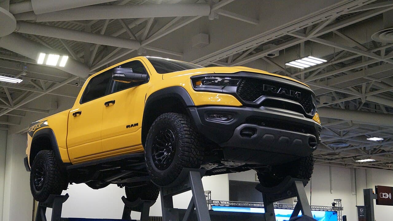 Low-angle front three-quarter view of a yellow Ram 1500 TRX raised on a display lift at the Twin Cities Auto Show, showing its underbody and off-road tires.